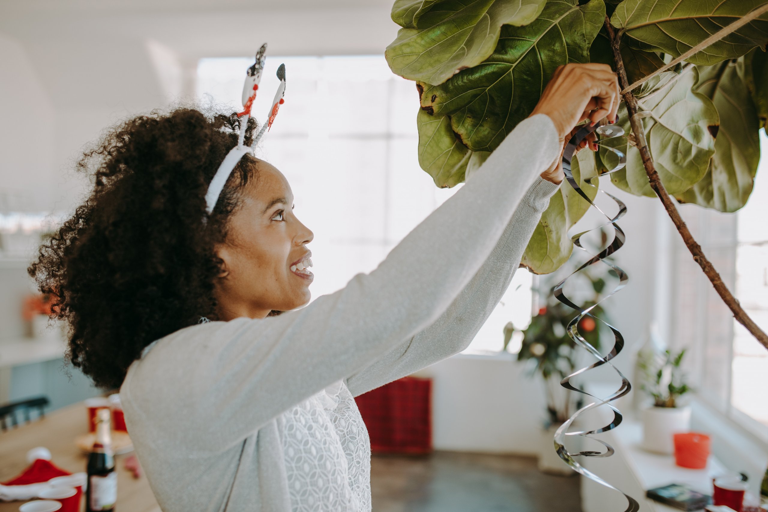 woman with snowman headband hanging silvers streamers from tall plants