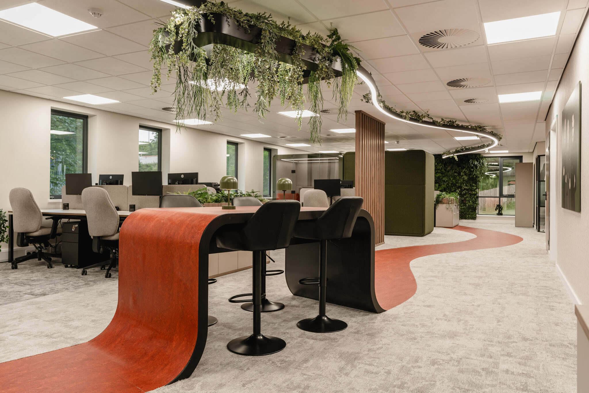 Curved orange poseur bar with stools at Bagnalls, set against the open-plan desks beneath a planted ceiling ring
