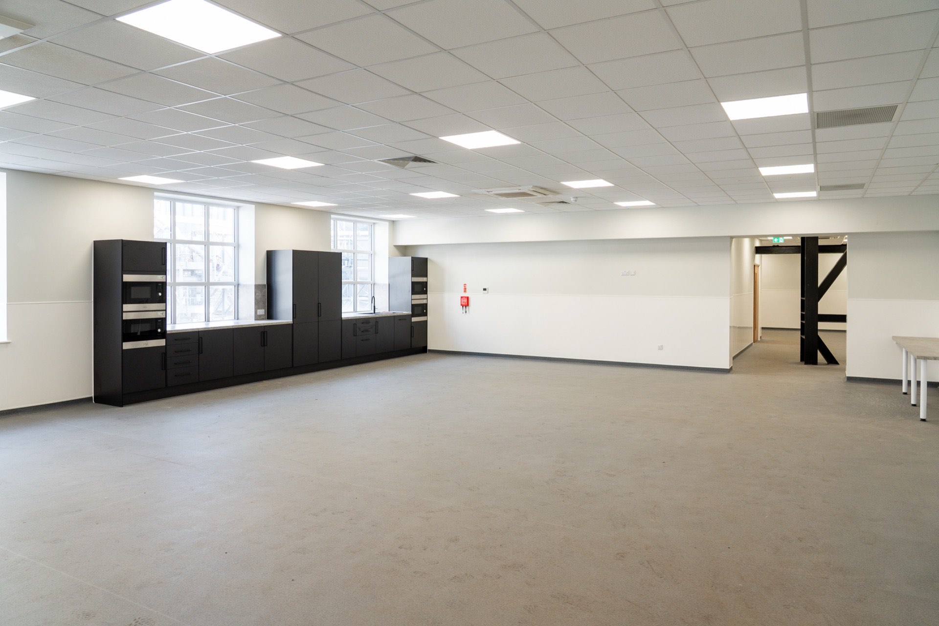 Breakout space at Breedon, with a fitted kitchen counter and an exposed dark timber portal-frame partition beyond