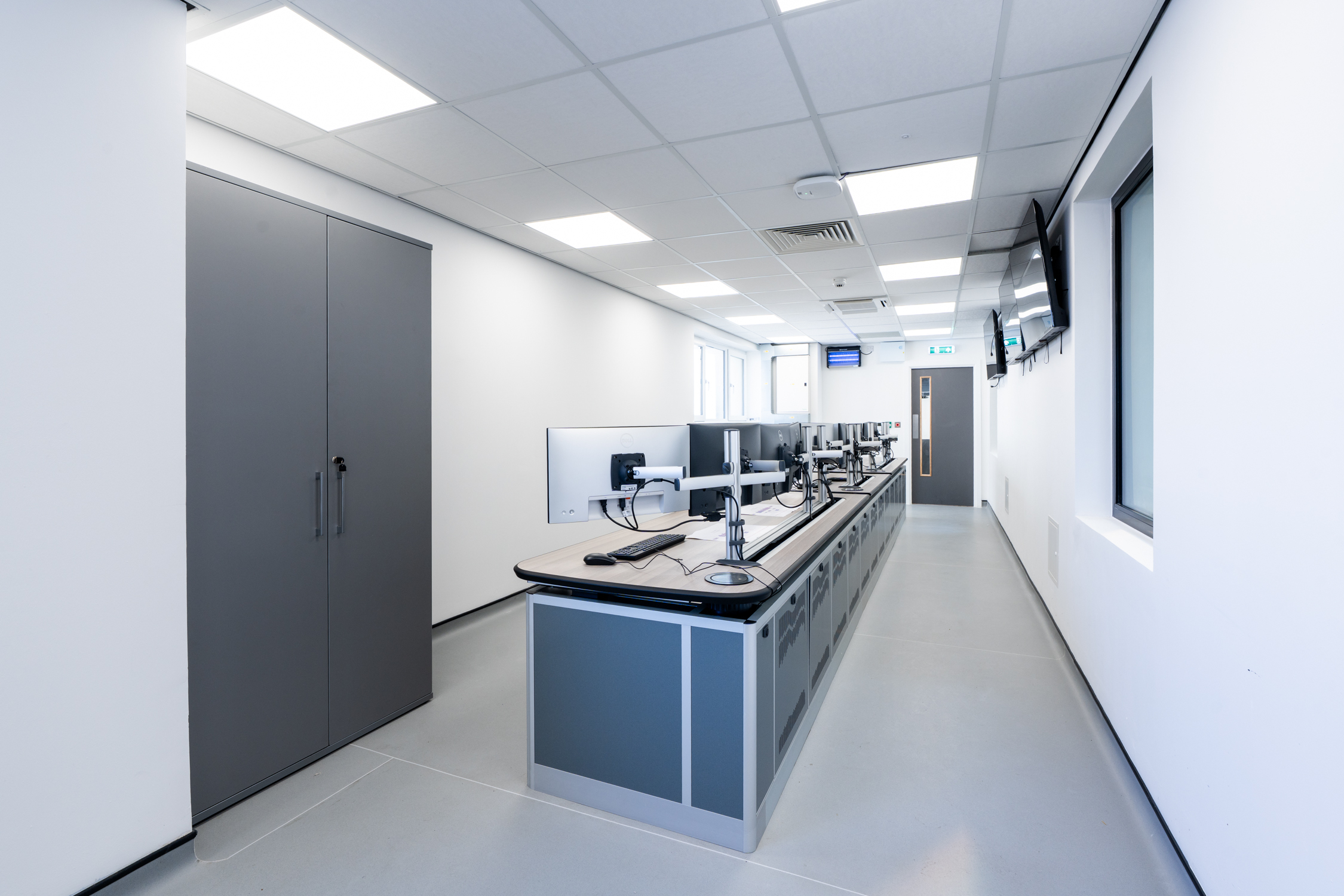 Control room desk at Cargill, a run of bespoke blue cabinetry carrying monitors on adjustable arms, with full-height storage alongside