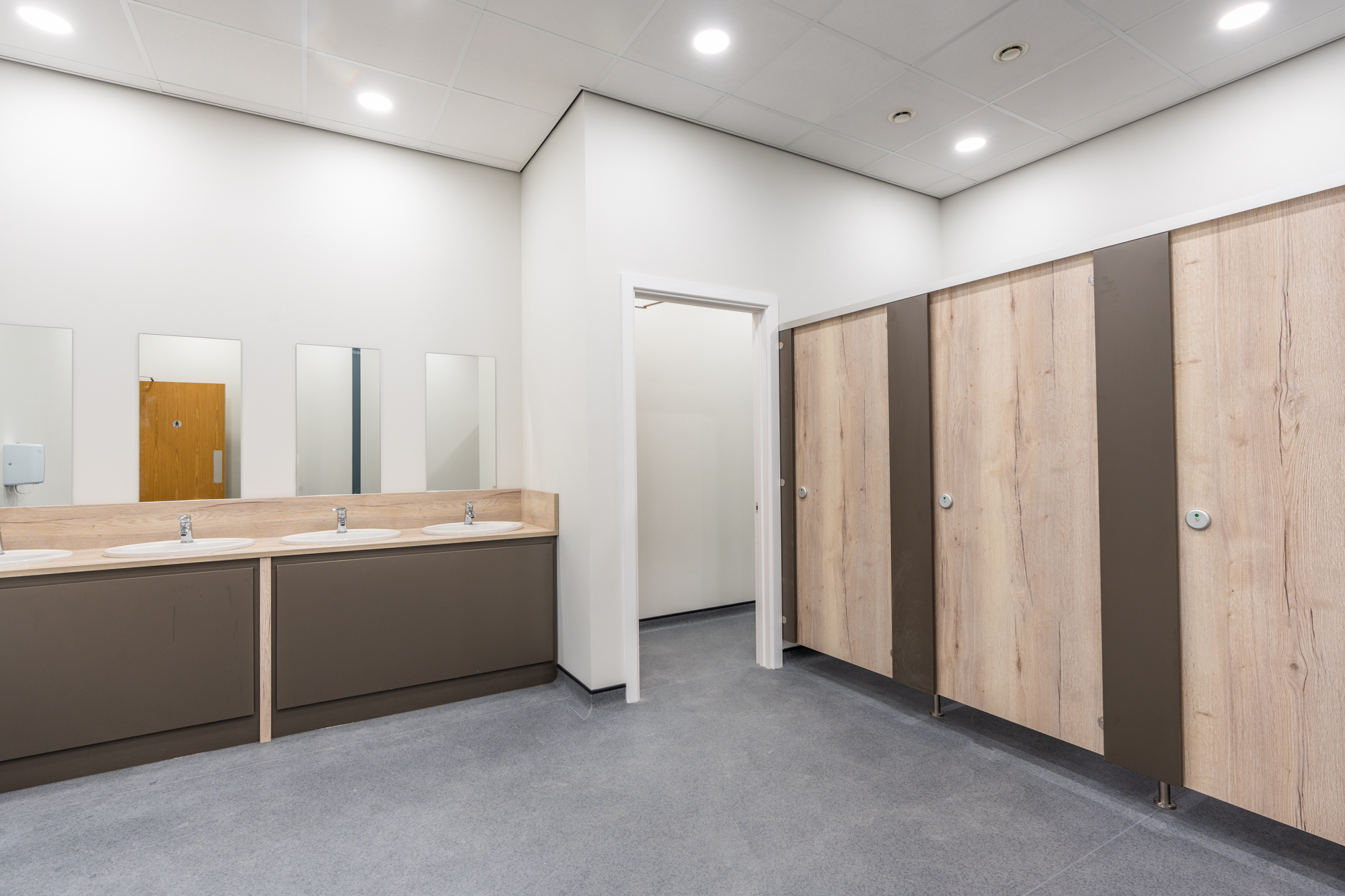 Washroom at Garolla, with a run of basins set into an oak-topped vanity below individual mirrors, and oak-effect cubicle doors opposite