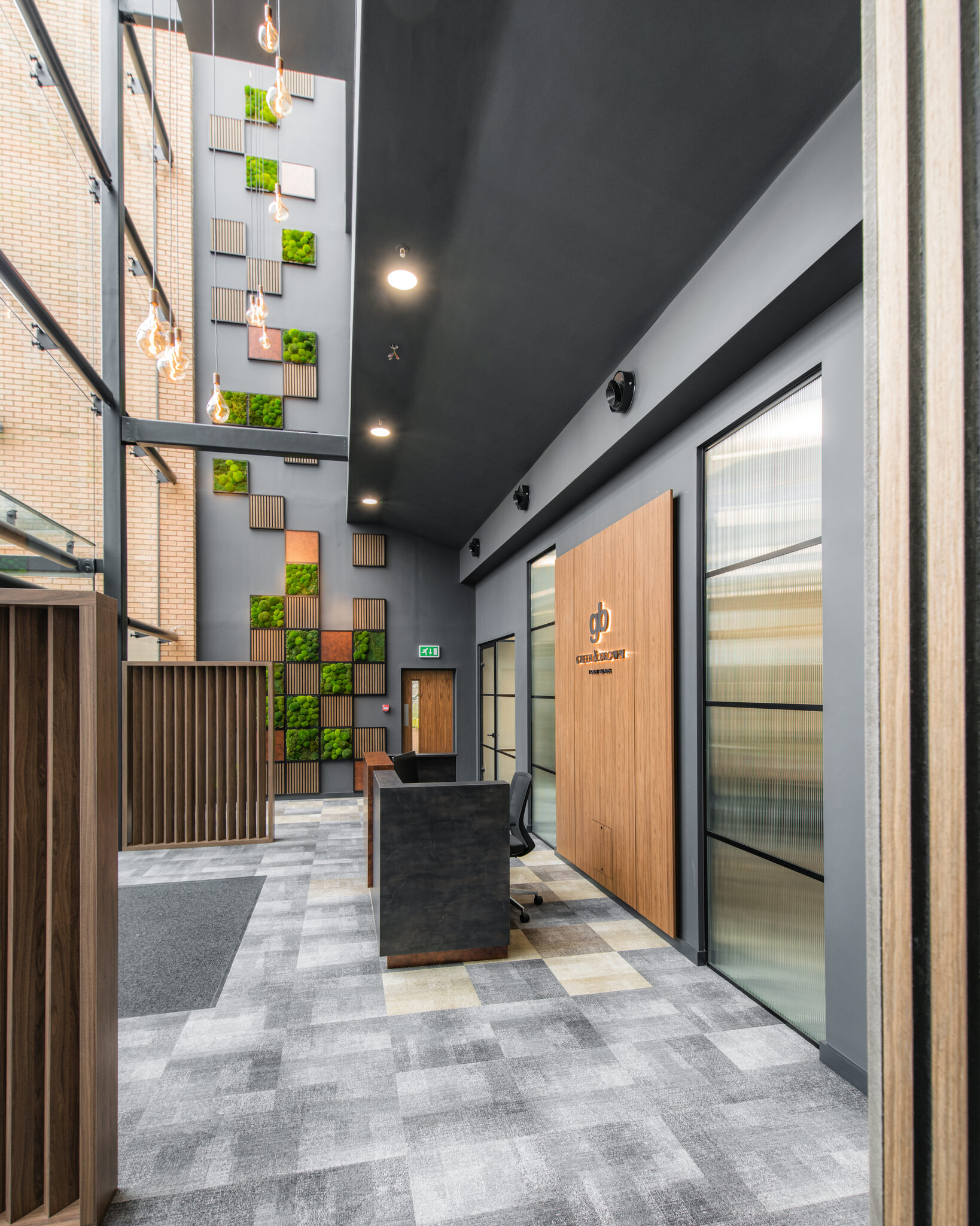 Entrance and welcome area at Green & Brown, a timber door and glazed partition beside a full-height feature wall of moss and tile panels