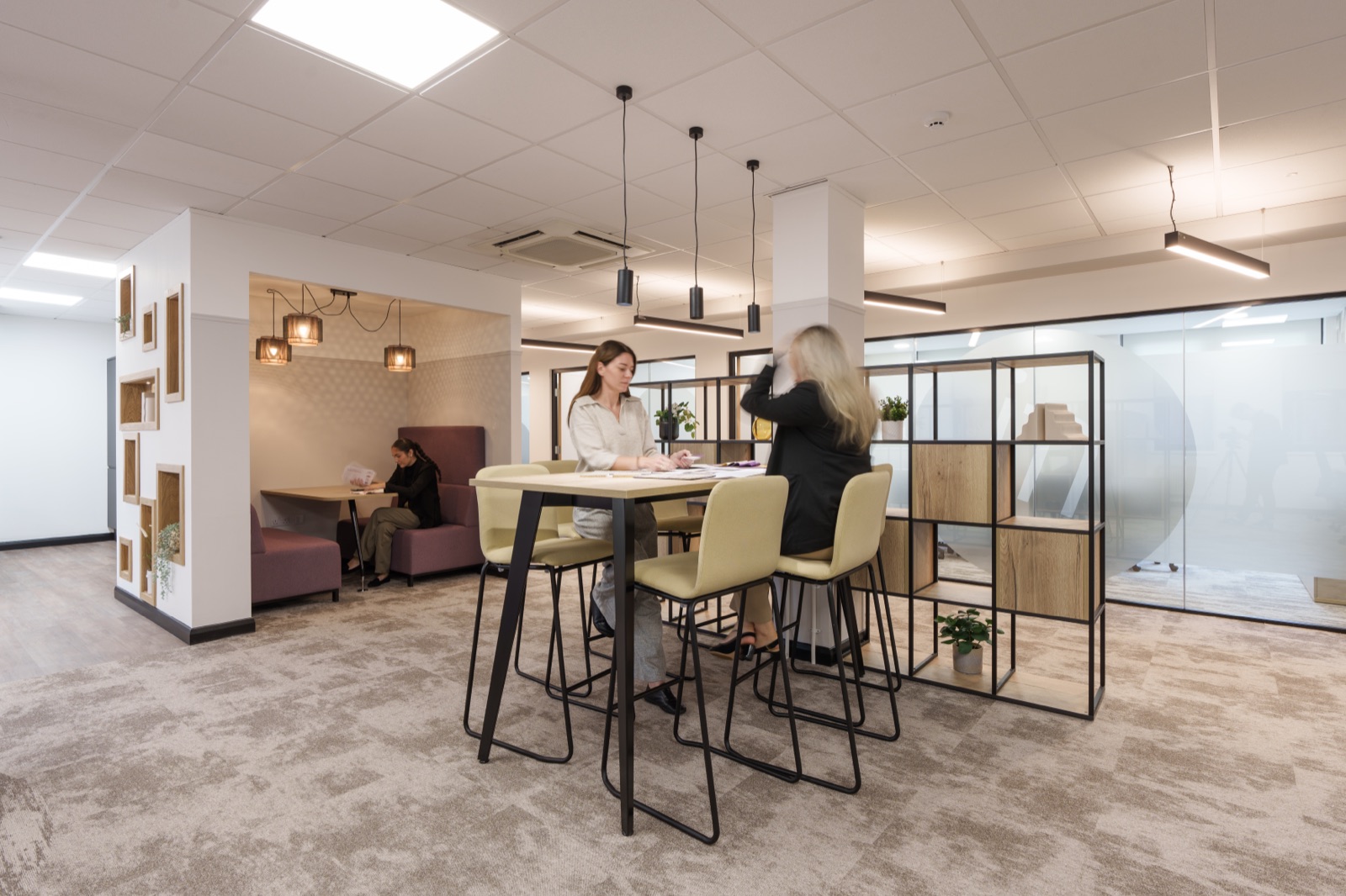 Colleagues working at a high table at Jones Myers in Leeds, beside a booth with cluster pendant lights and an open timber-frame divider