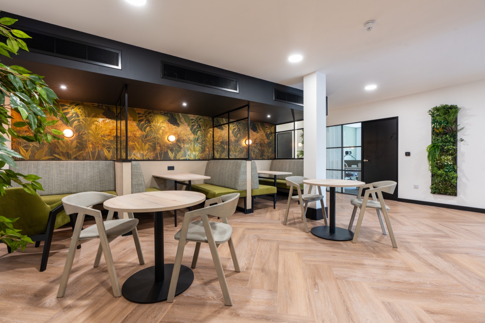 Breakout booths at Morson Group with olive-green banquette seating against a gold tropical mural, and a living moss panel beyond