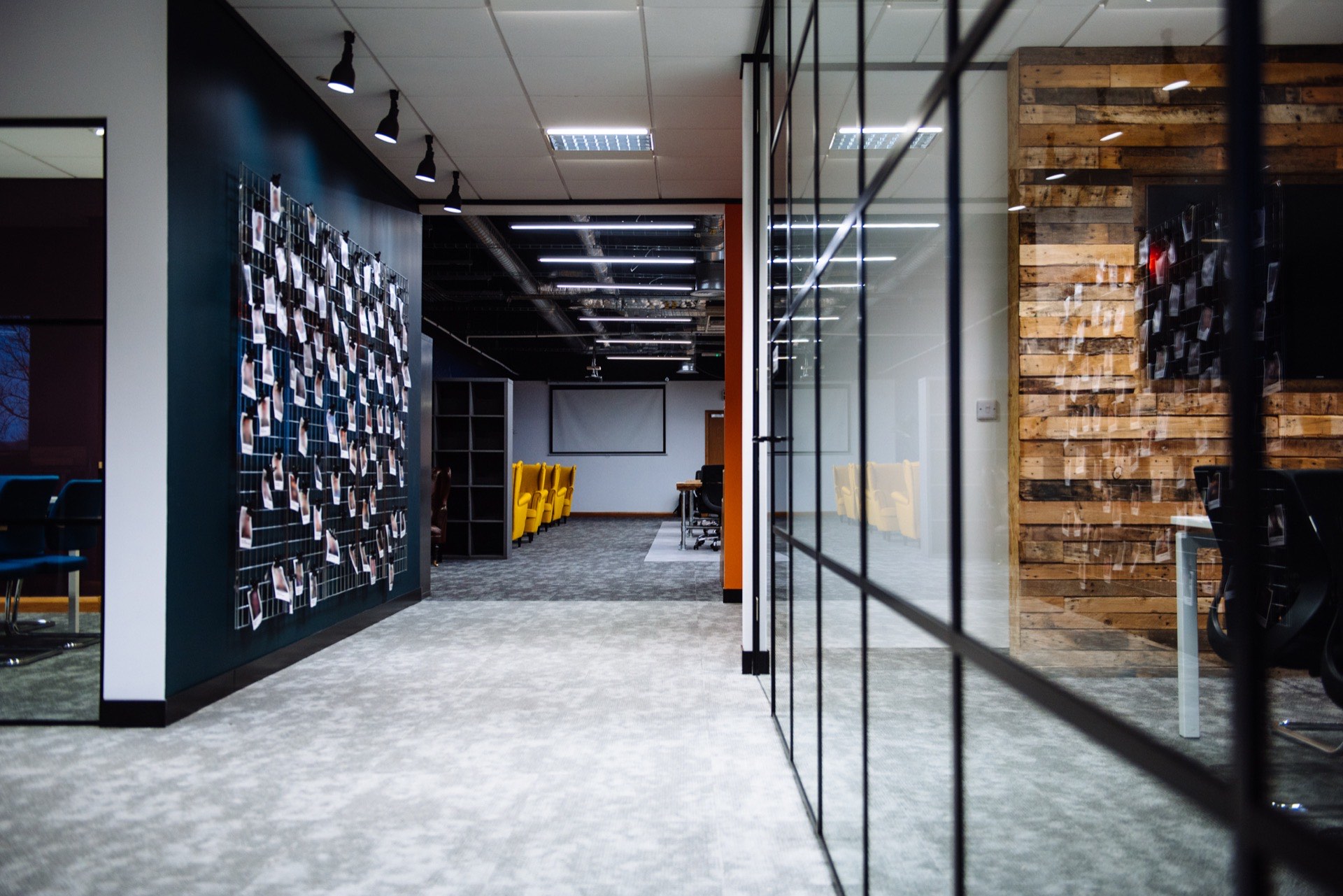 Breakout corridor at Quality Bearings Online, with an exposed dark ceiling, pendant lighting and a project photo wall