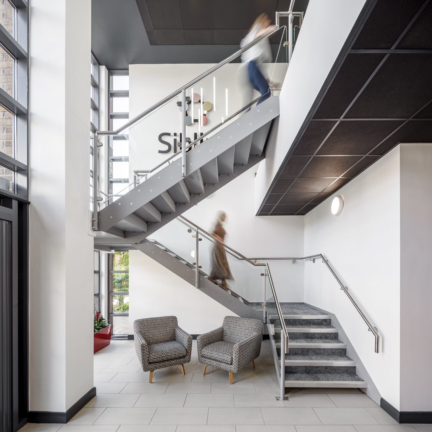 Double-height reception foyer at Sibling Workspace, with a feature staircase and armchairs below