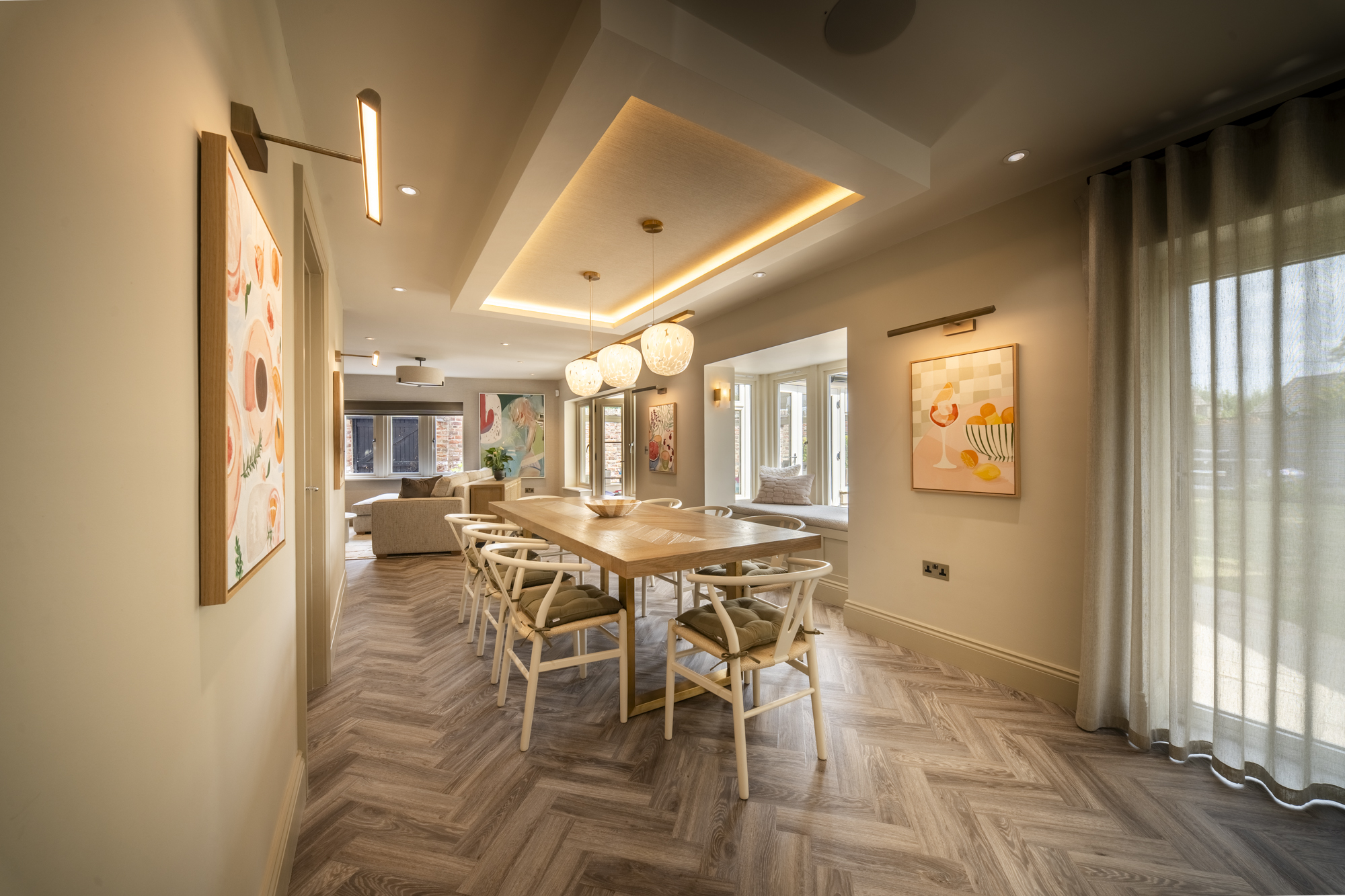 Open-plan dining and living space at Well House, with a herringbone floor, recessed illuminated ceiling and a bay window seat beyond