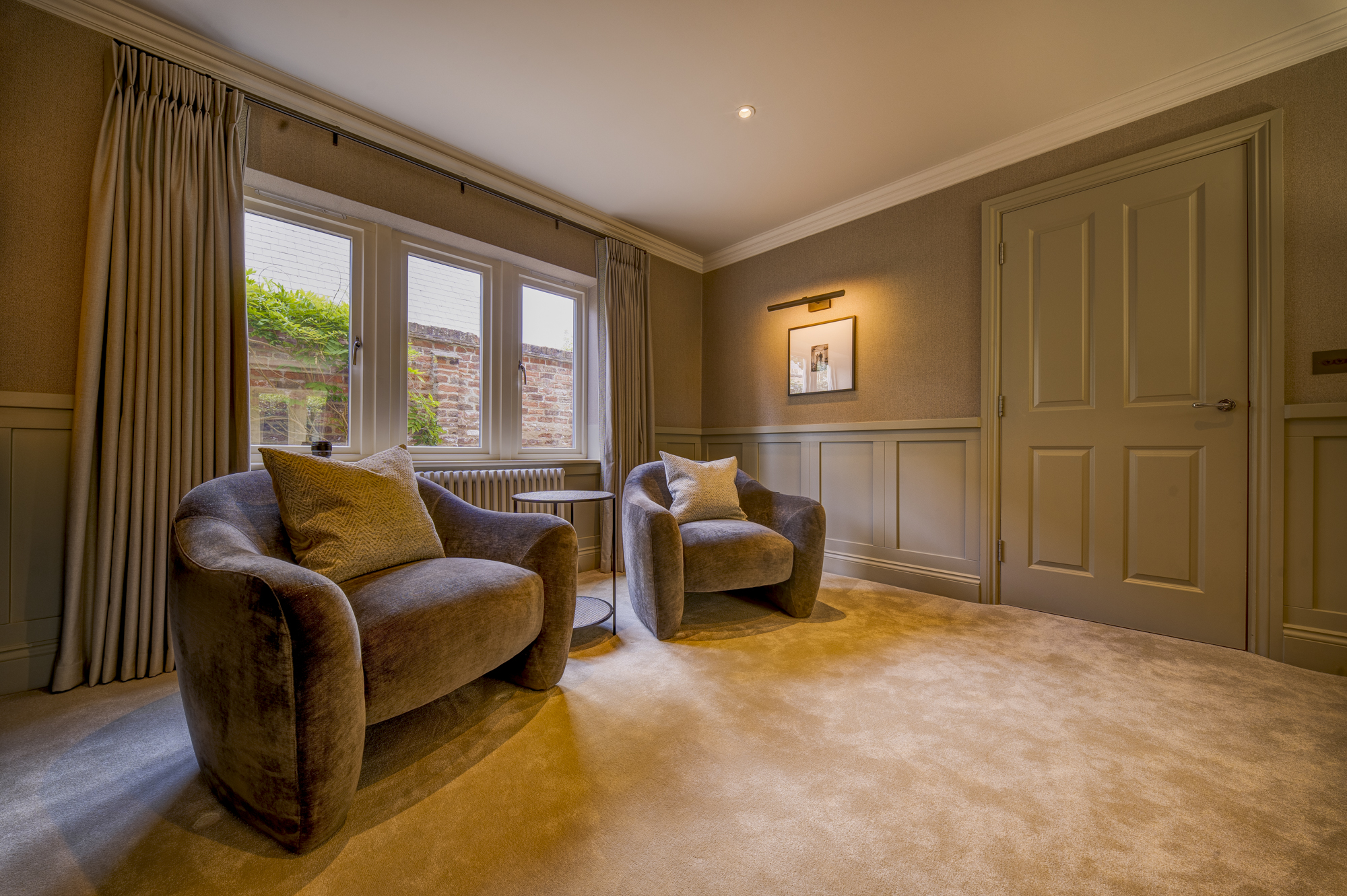 Refurbished sitting room at Well House with curved velvet armchairs beside a mullioned window